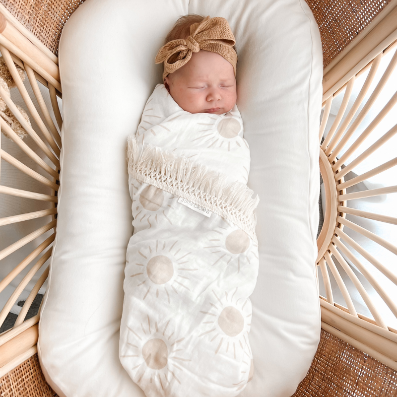 Newborn in bassinet swaddled with Sun Fringe Swaddle Blanket