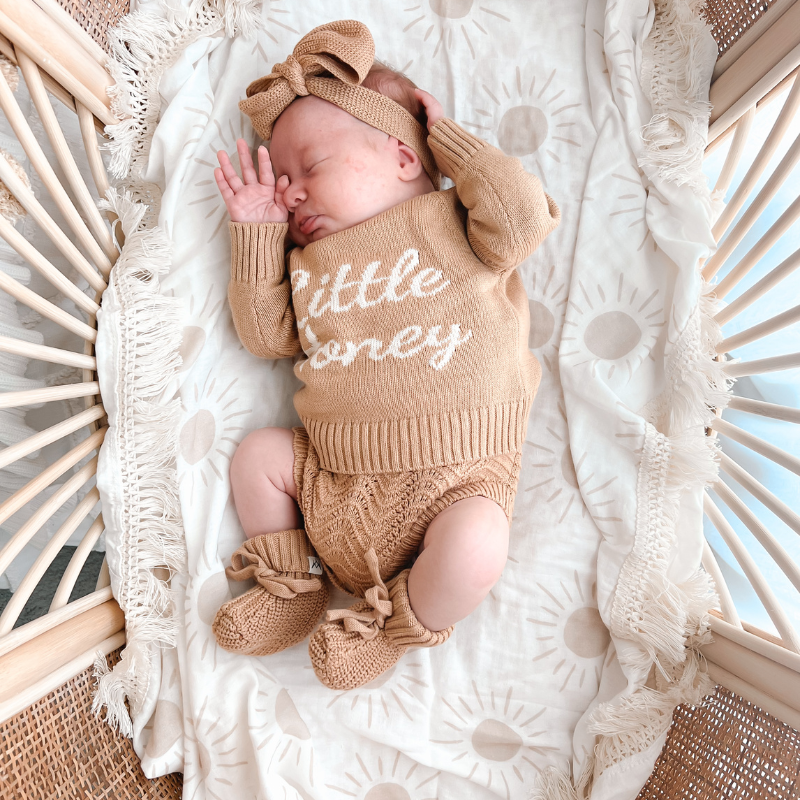 Shy newborn laying in bassinet on top of Sun Fringe Swaddle Blanket