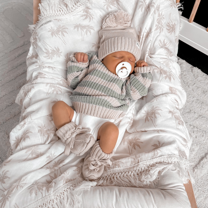 Baby with dummy asleep on the palm fringe swaddle blanket
