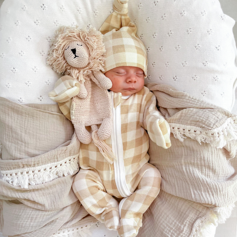 Gingham My First Outfit with Beanie on Baby lying on a swaddle with Lion Cuddle Me Comforter