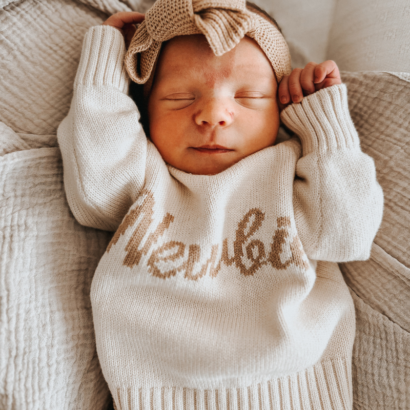 Newborn baby with hands by their head wearing a Newbie Jumper