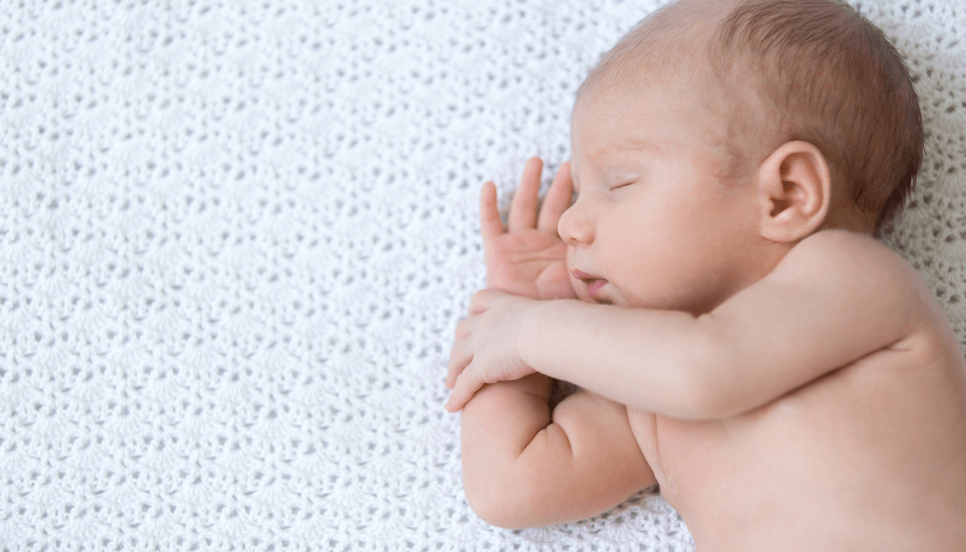 Newborn baby asleep on the knitted white blanket