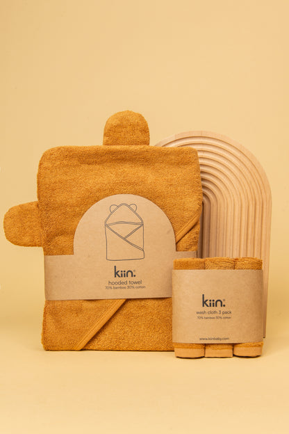 Caramel Hooded Towel and matching face cloths in packaging standing up against a wooden rainbow