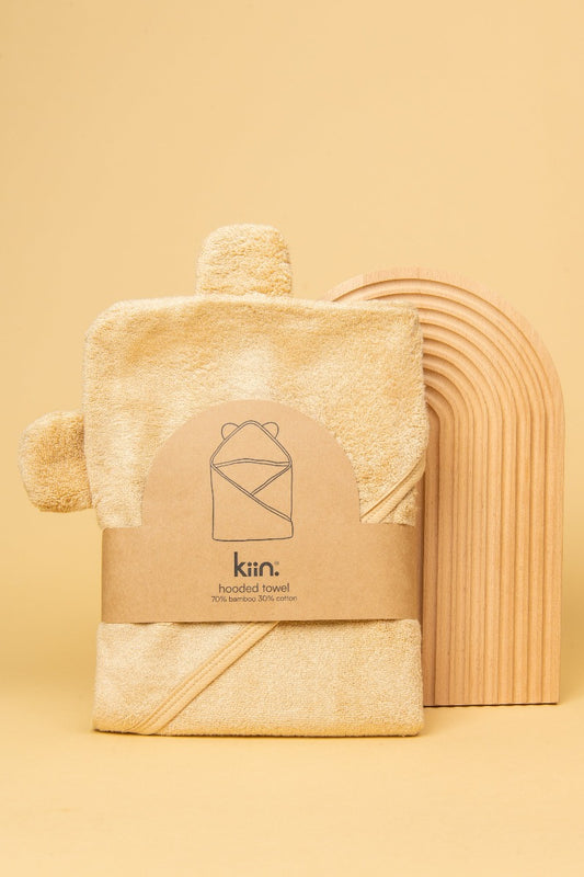 Oat Hooded Towel in packaging standing up against a wooden rainbow