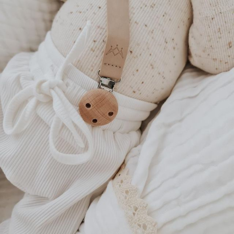 3 little crowns vegan leather dummy clip in nude with wooden clip attached to newborn baby's pants