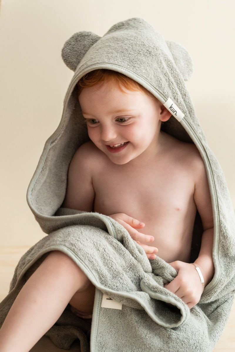 Cute little boy using the Kiin Baby Hooded Towel Sage