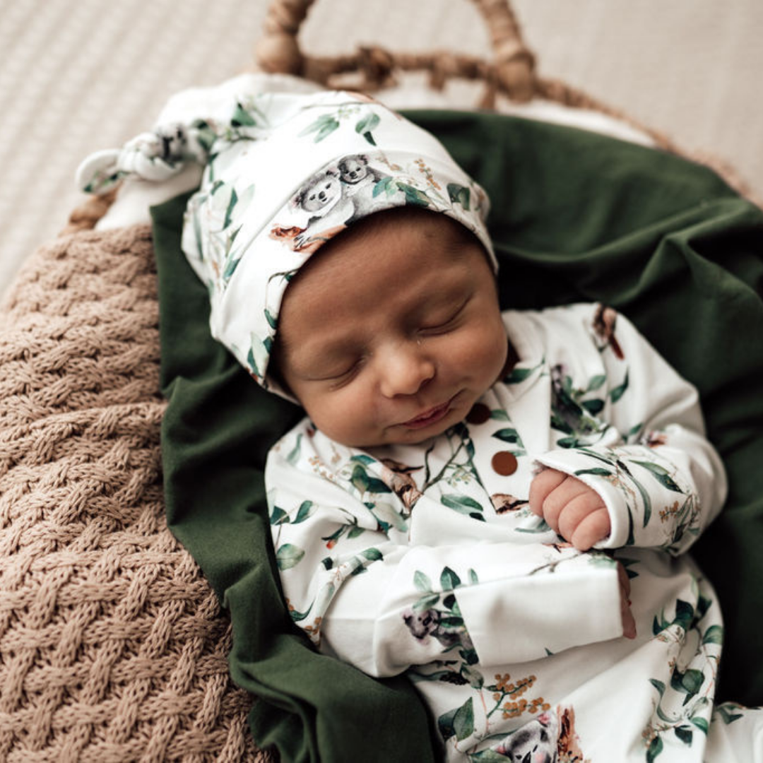 Snuggle Hunny Kids Knotted Beanie Eucalypt Baby with matching growsuit lying on green blanket in moses basket