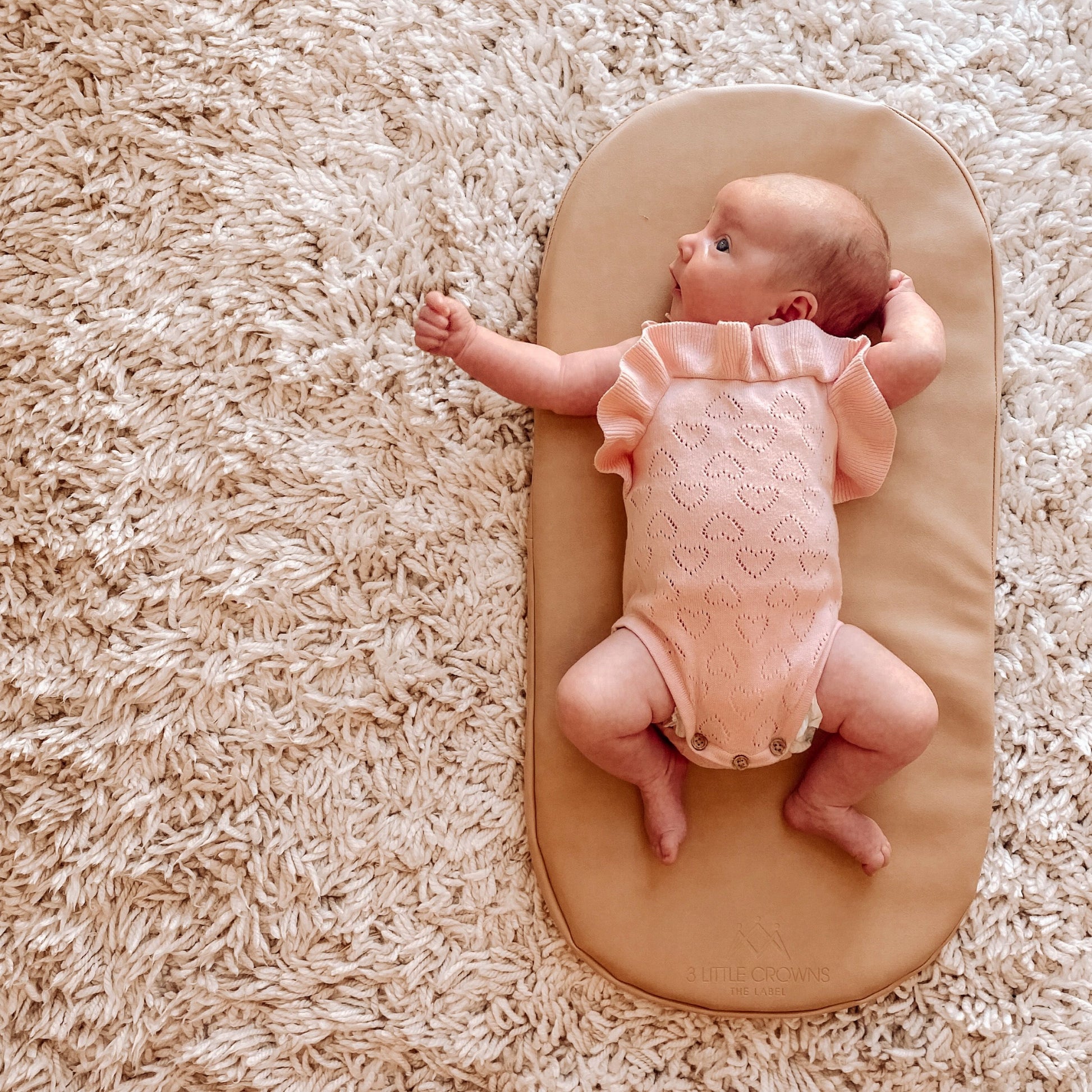 Newborn baby lying on nude vegan leather change pad on white wool carpet